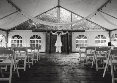 Outdoor wedding ceremony tent with chairs and floral decor.
