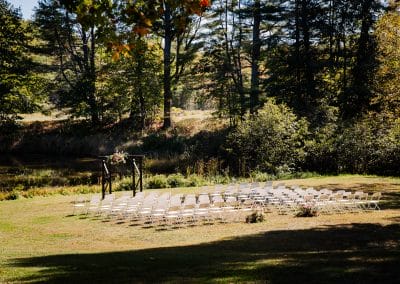 Outdoor wedding ceremony setup with chairs and floral arch in a lush forest setting.