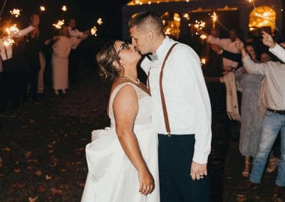 Romantic wedding couple sharing a kiss at Lupines & Lace outdoor venue with string lights.